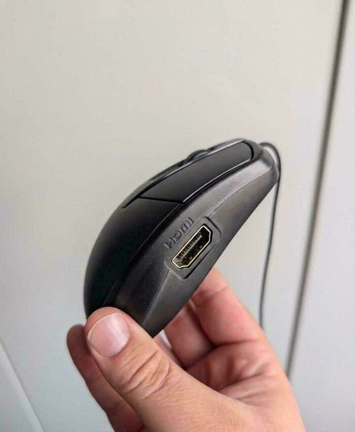 A hand holding a peculiar computer mouse with an HDMI port on its side.