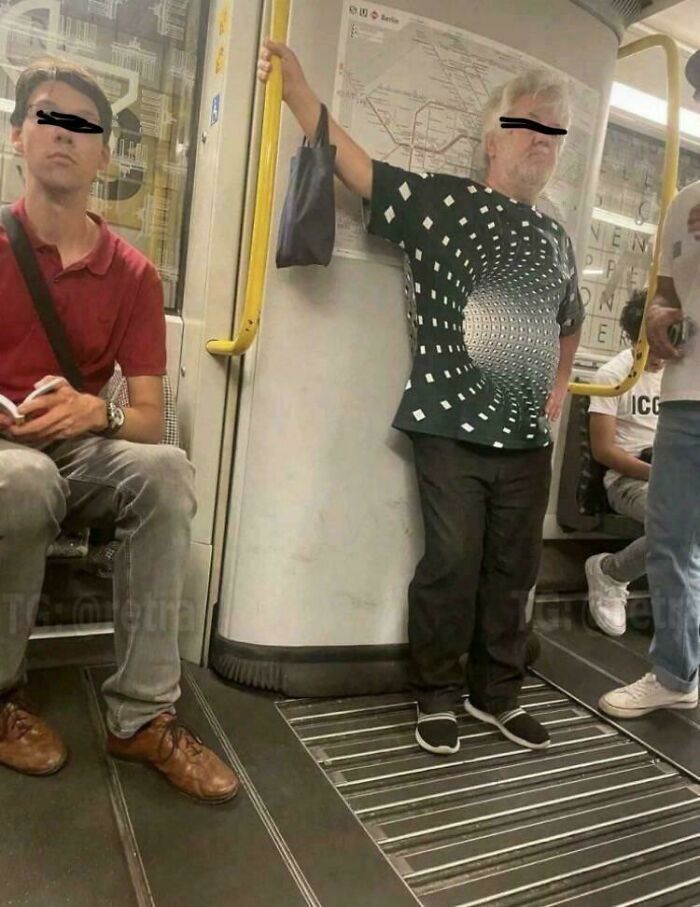 A peculiar man on a train wearing an optical illusion shirt that makes his torso appear to have a black hole, a real-life sight.