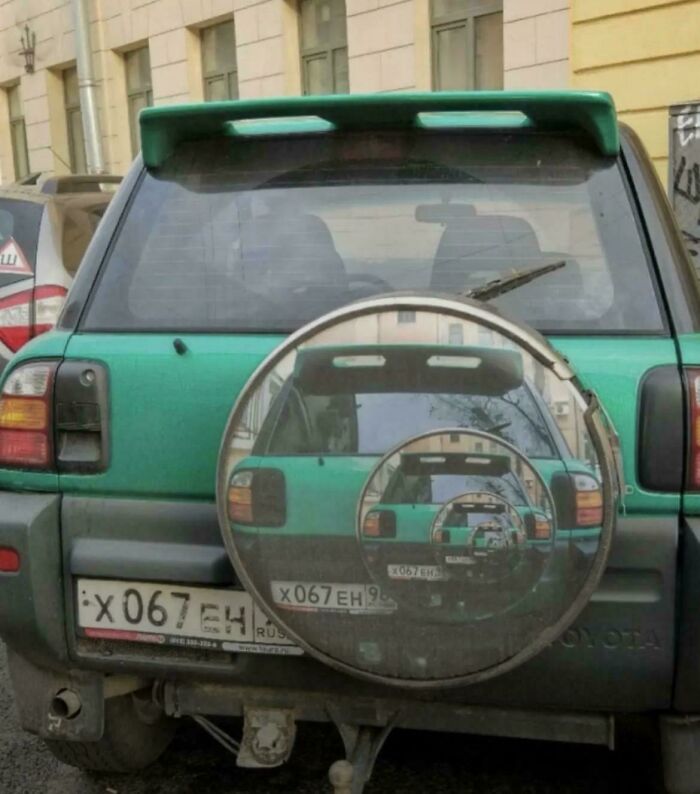 Green SUV with a spare tire cover showing a recursive image, a peculiar thing spotted in real life.