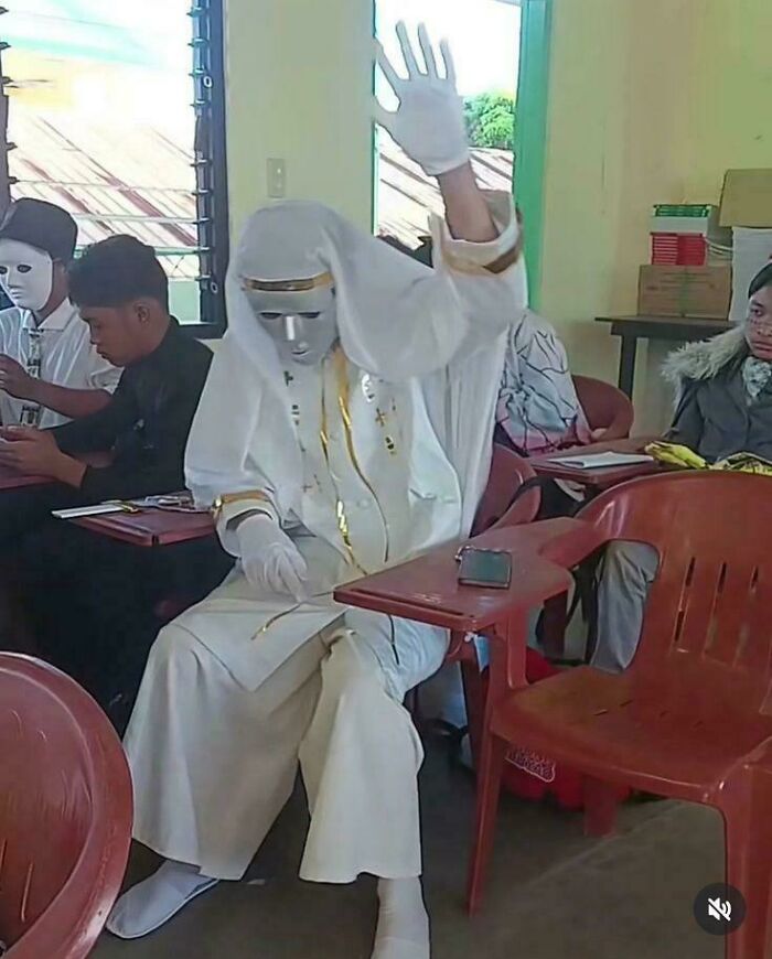 Student in white robes and a mask raising a hand, a peculiar thing spotted in real life.