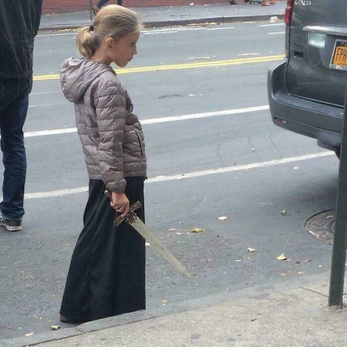 Peculiar things spotted in real life: A young girl in a long skirt and jacket holding a sword on a city street.