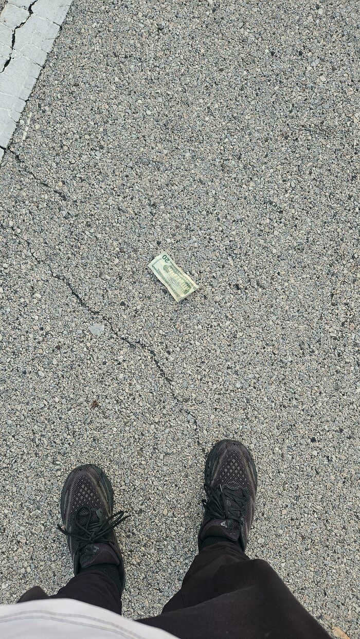 A pair of black shoes standing over a crumpled twenty-dollar bill on the ground, a Not Interesting community photo.