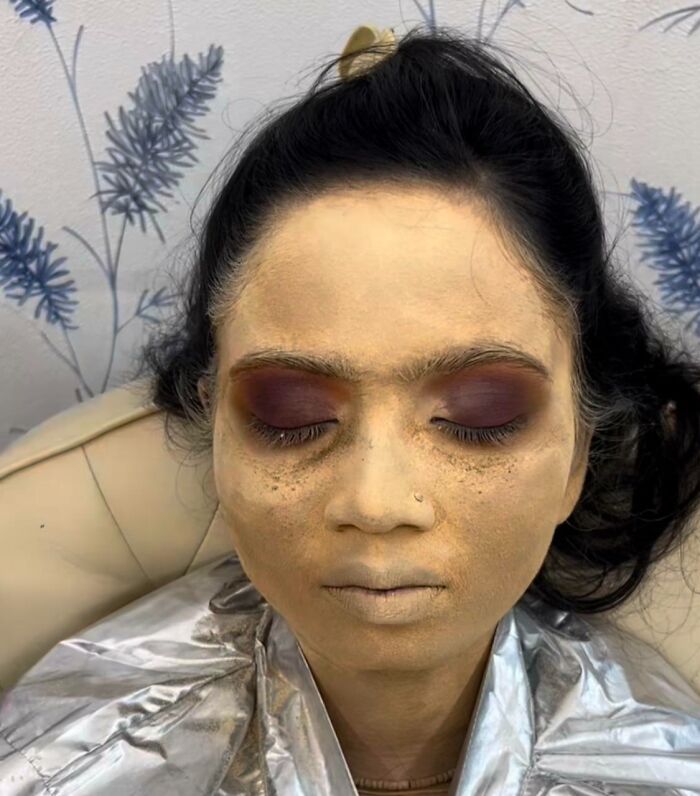 A woman with badly applied makeup at a beauty salon, looking worse with thick, uneven foundation and dark eyeshadow.