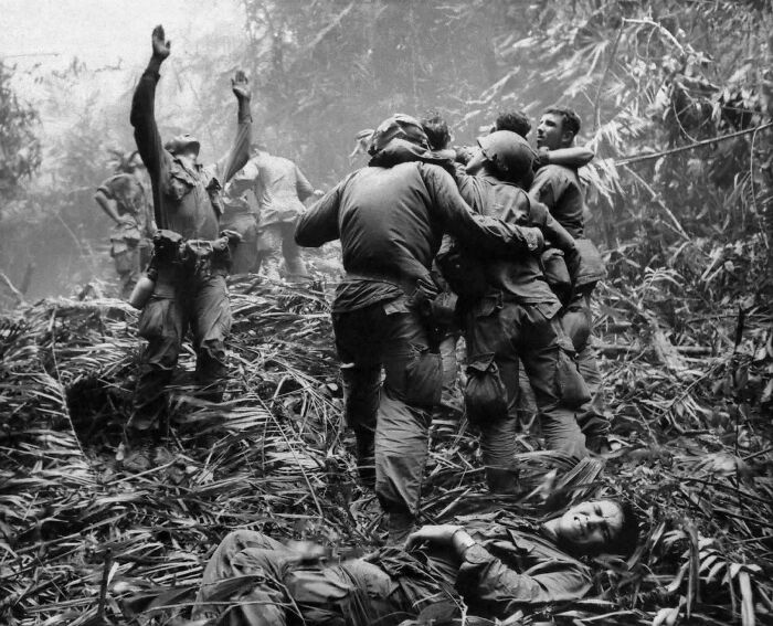 Soldiers in a jungle, one with hands raised, another on the ground in a powerful historical photo with emotional depth.