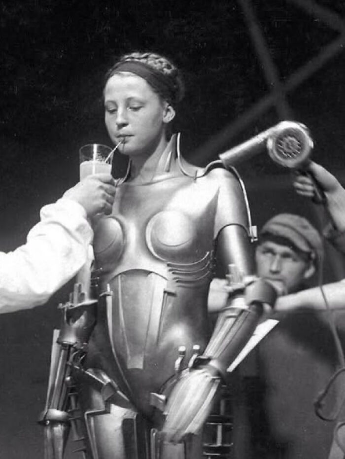 Historical photos of actress Brigitte Helm in her robot costume from the film Metropolis, drinking through a straw.