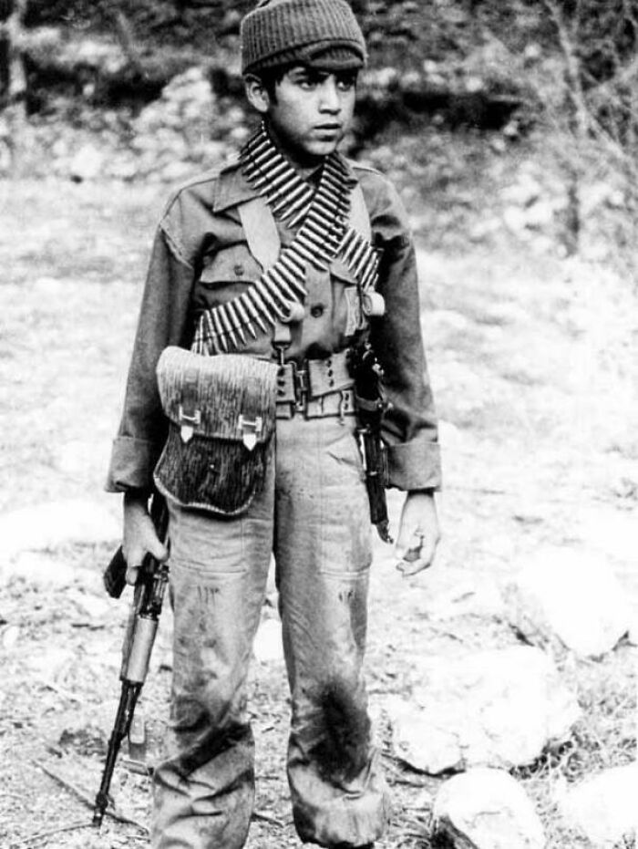 A young boy in military attire holding a rifle, representing a poignant moment in historical photos.