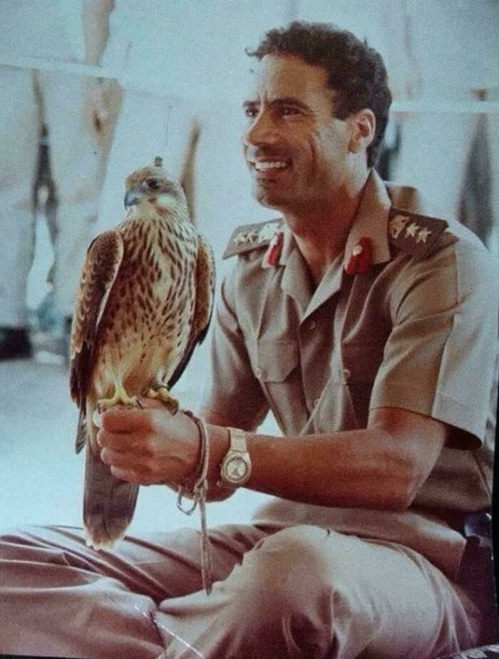 A smiling man in uniform holds a falcon on his arm, a fascinating historical photo.