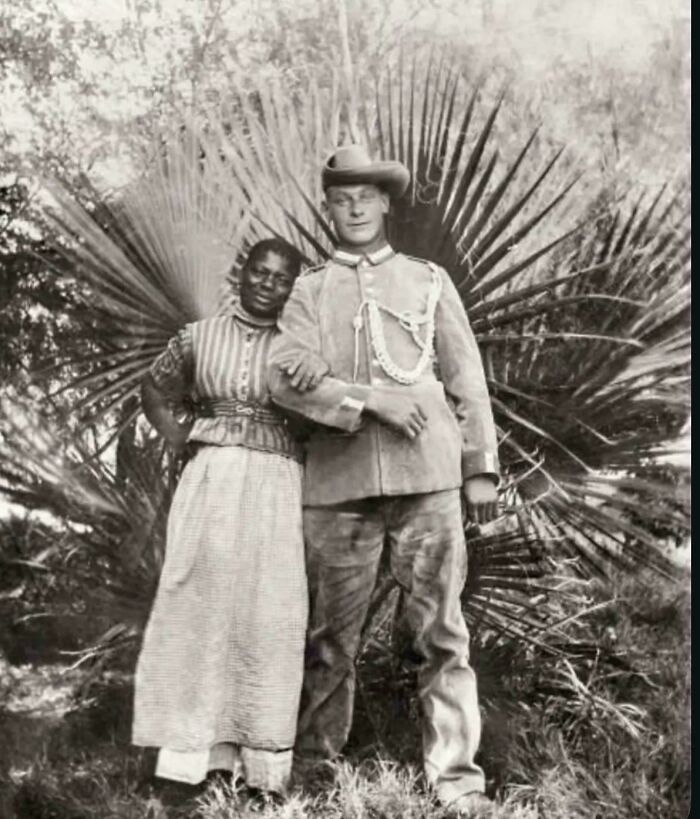 A black and white historical photo shows a couple, a man in military uniform and a woman, standing together.