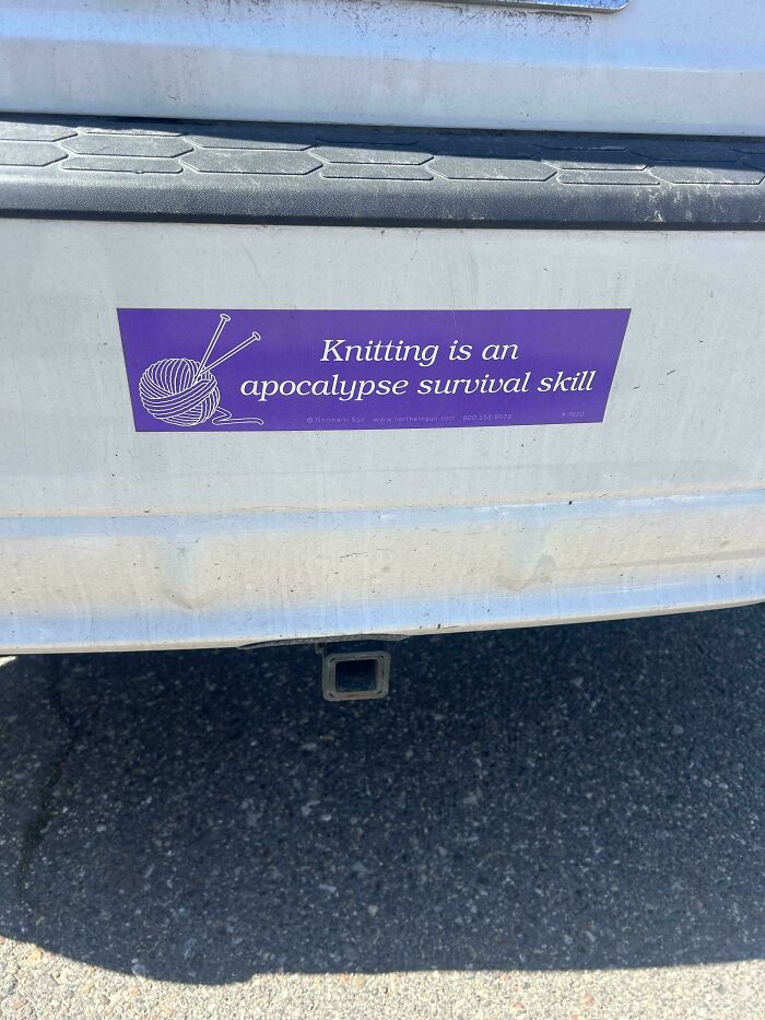 A silver car's bumper featuring a funny bumper sticker that reads: Knitting is an apocalypse survival skill.