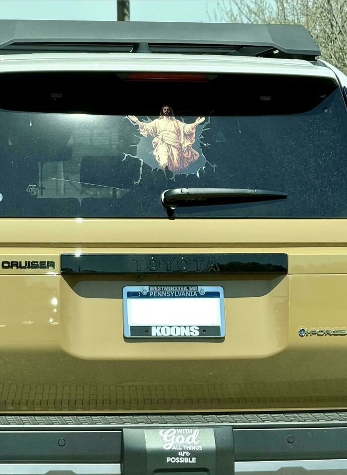 Wild bumper sticker on a gold Toyota showing Jesus breaking through the back window.