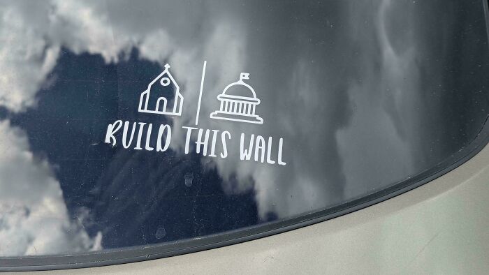 A funny bumper sticker on a car window with a church and Capitol building, reading Build This Wall.