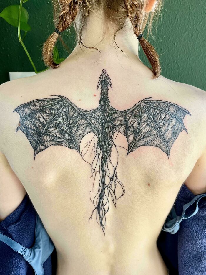 A stunning back tattoo of a detailed dragon with large, textured wings and a long, flowing tail.