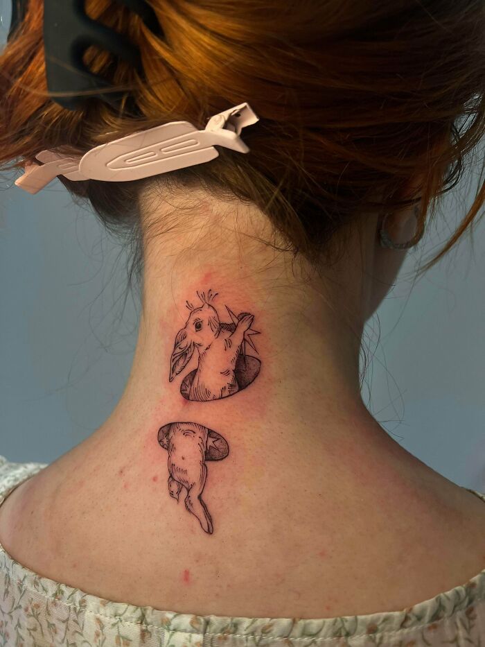 Two small rabbit tattoos on the back of a neck, one peeking out and one disappearing, lovely stunning tattoos.