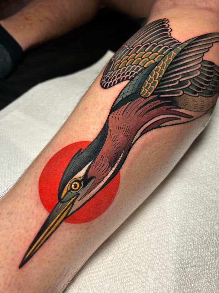 A vibrant bird tattoo with a red circle background on someone's leg, showcasing stunning tattoos.