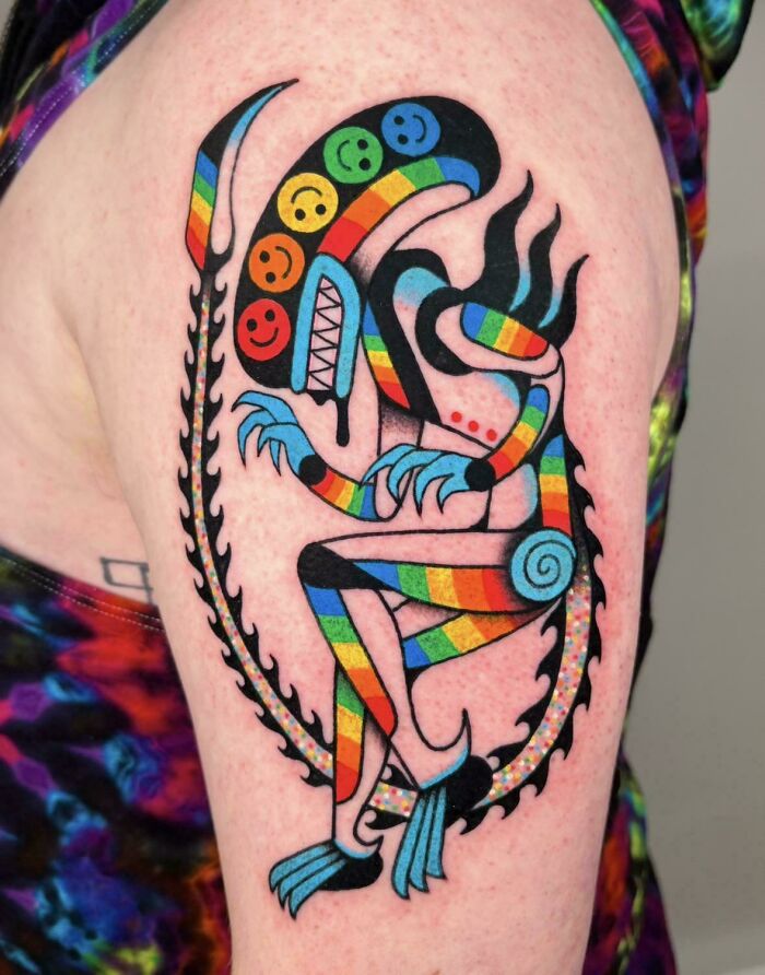 A vibrant, colorful rainbow alien tattoos on an arm, featuring various smiley faces on its head. Stunning tattoo.