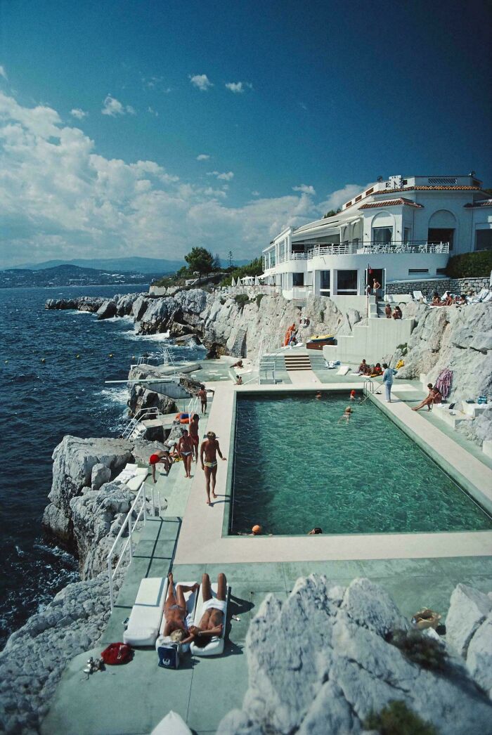 Vintage coastal swimming pool with people sunbathing and enjoying the ocean view on rocky cliffs