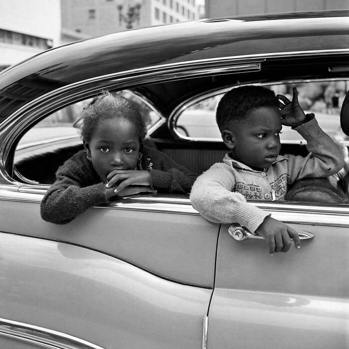 Black and white portrait of two children leaning out of vintage car window