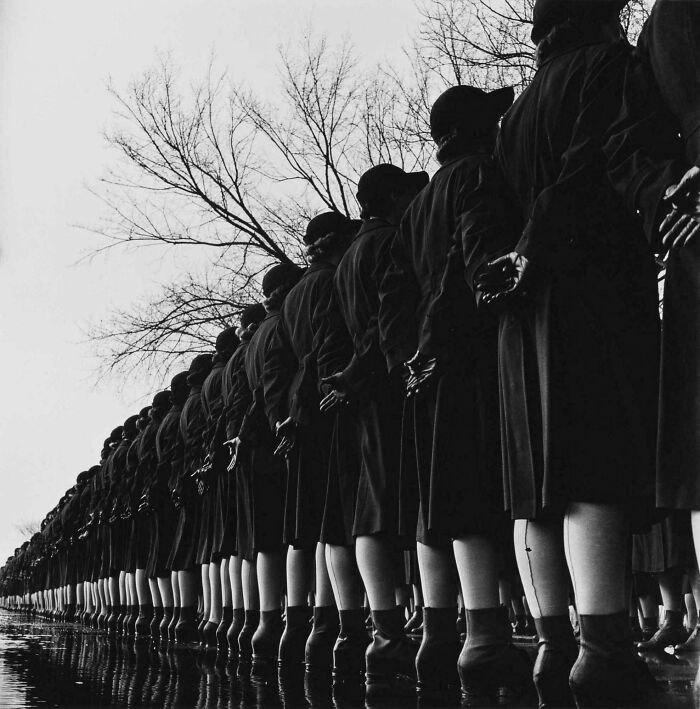 Black and white vintage photo of women standing in line with hands behind back