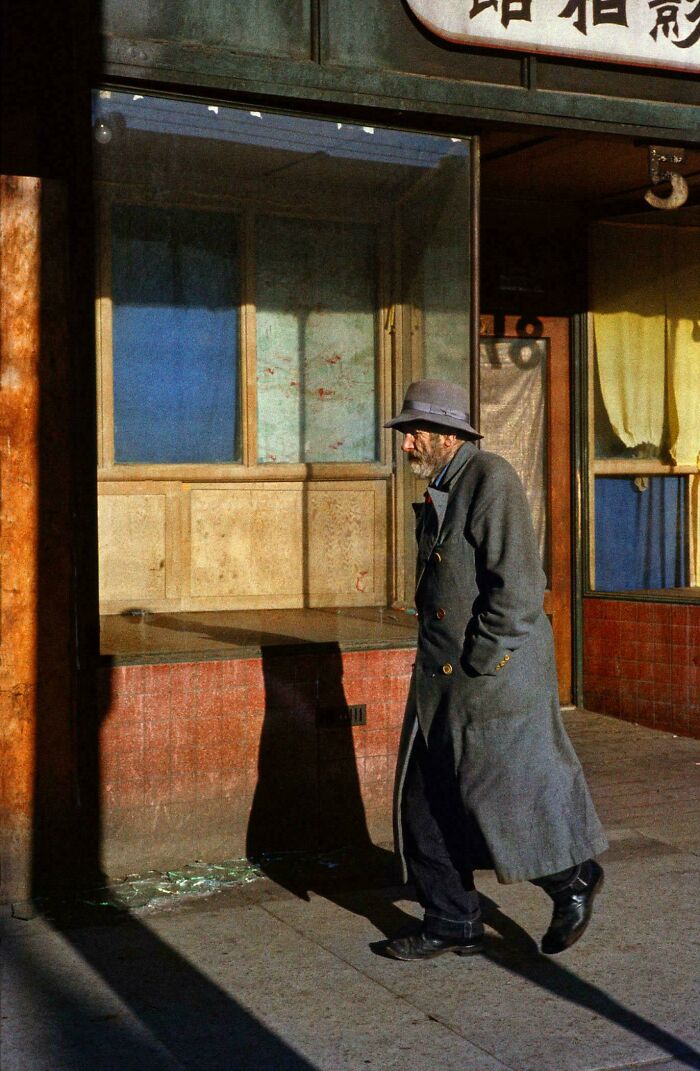 Older man in long coat walking past old storefront in nostalgic real photo