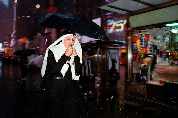 Woman dressed as nun holding umbrella on rainy city street in real candid photo