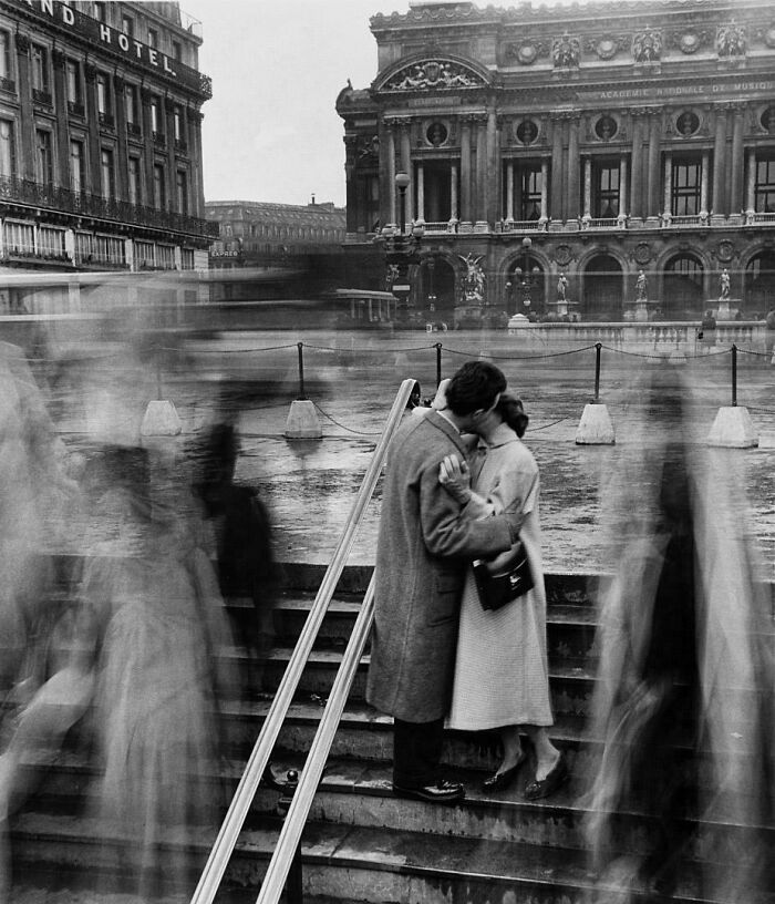 Couple kissing on city steps with blurred pedestrians around