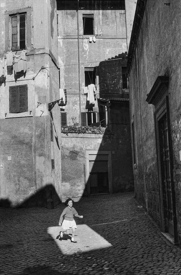 Black and white photo of a child running on a cobblestone street with laundry hanging in shadows
