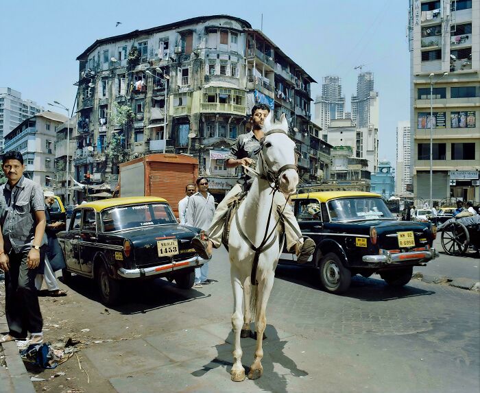 Man riding white horse in busy city street with taxis nearby