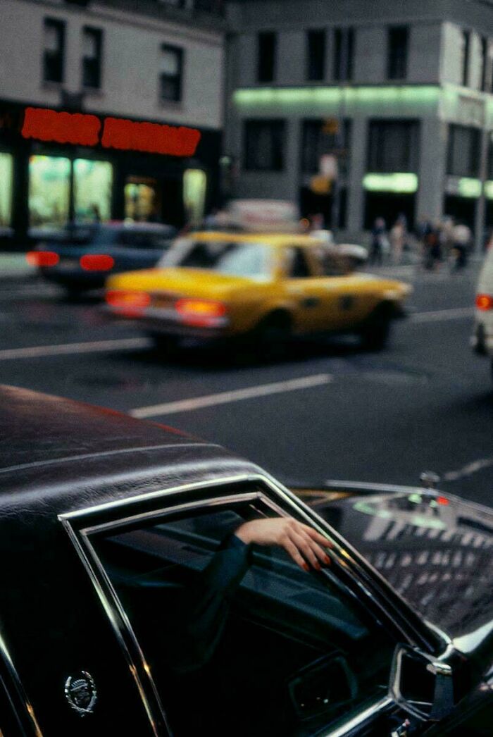 Close-up of hand out car window with yellow taxi in city traffic