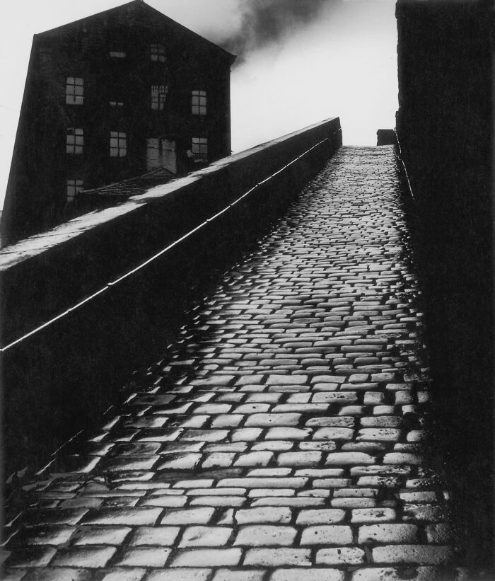 Historic black and white photo of cobblestone street with factory and smoke
