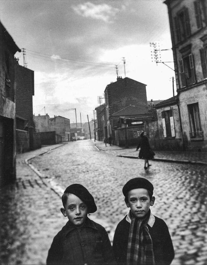 Black and white photo of two boys in berets on a cobblestone street with buildings
