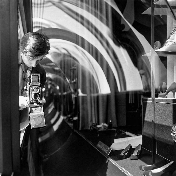 Old black and white photo of woman taking a photo through glass in a shoe store