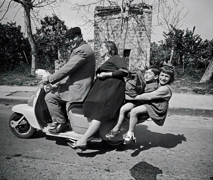 Retro black and white photo of a family riding crowded scooter on a sunny street