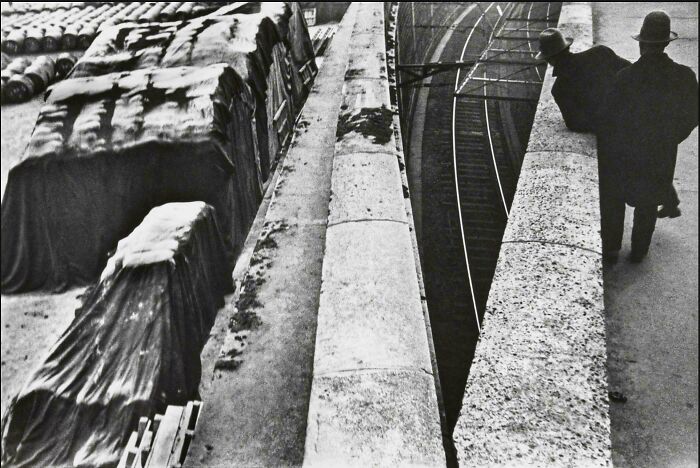 Old black and white street photo showing two men walking by a curved bridge over railway tracks