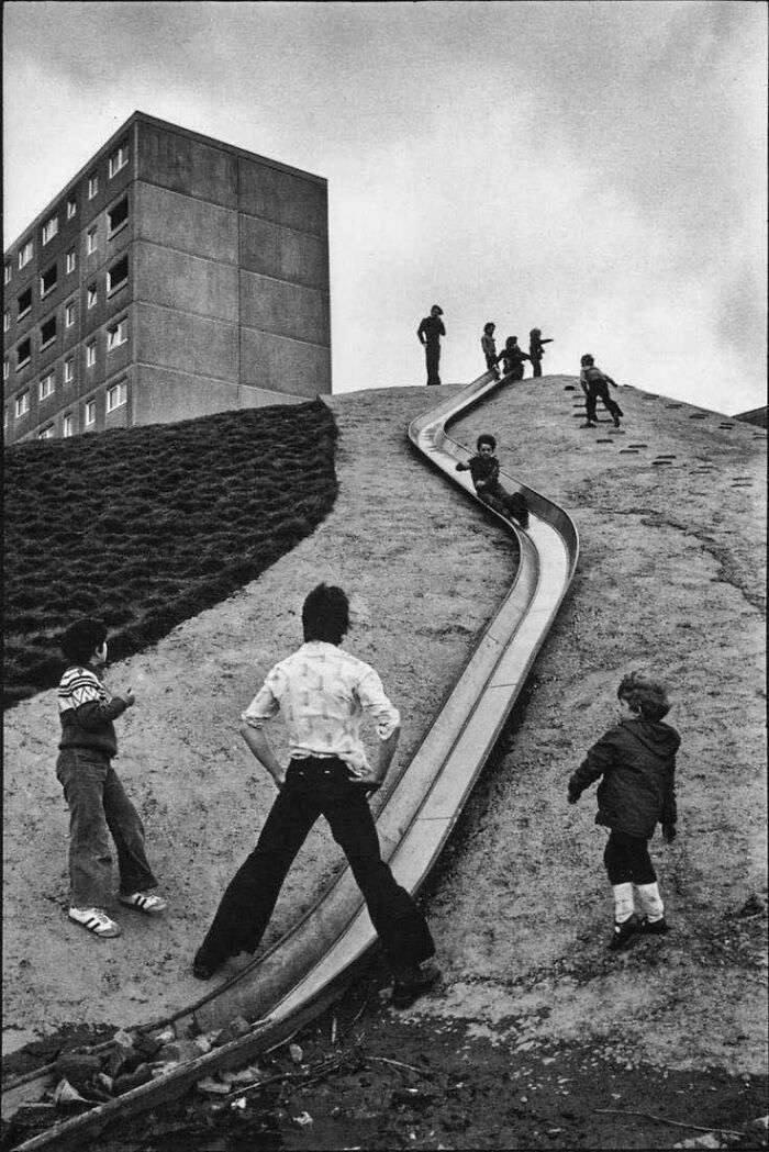Vintage photo of children playing on an outdoor slide in front of an apartment building