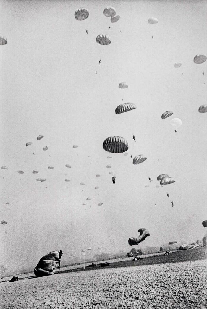 Black and white historic photo of numerous parachutes descending over a field during military exercise