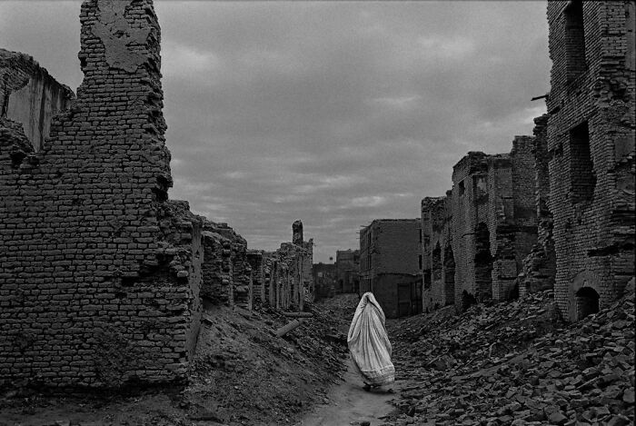 Person in white robe walking through ruins of destroyed buildings