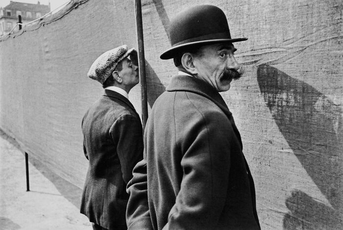 Two men in vintage hats looking at something behind a fence