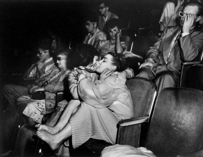 Couple kissing in a crowded theater watching 3D movie with others wearing 3D glasses