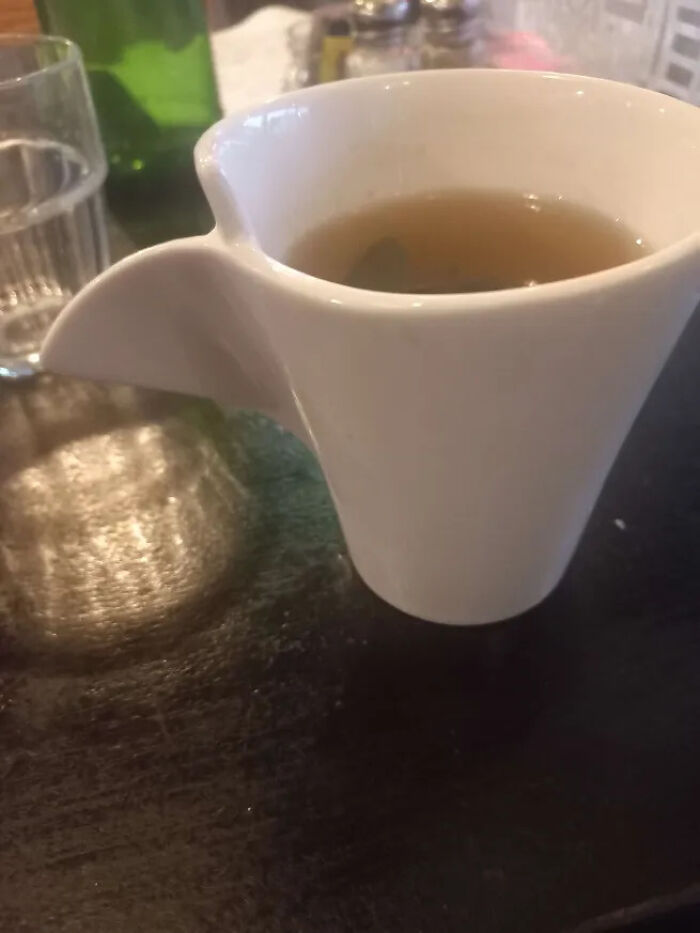 White ceramic cup with unconventional handle design holding tea on table