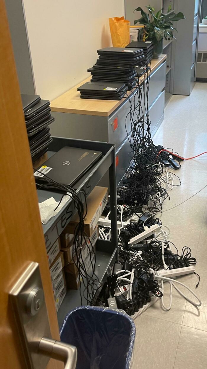 A room with numerous laptops and an overwhelming pile of tangled electronics cables on the floor, showing electronics fails.
