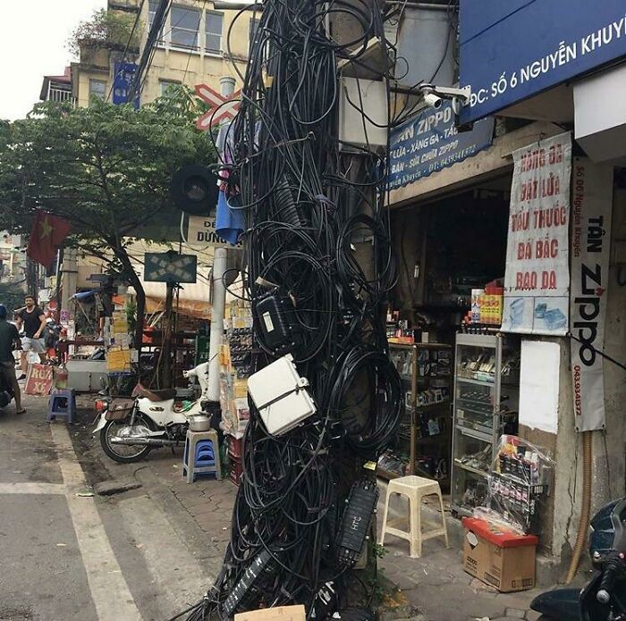 An outdoor pole completely covered in a chaotic tangle of electronics wires, a clear electronics fail.