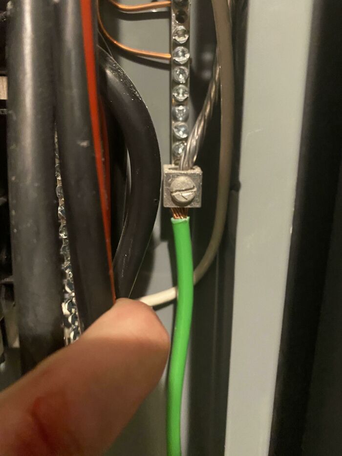 A finger pointing to a loose green wire in an electrical box, showcasing electronics fails.