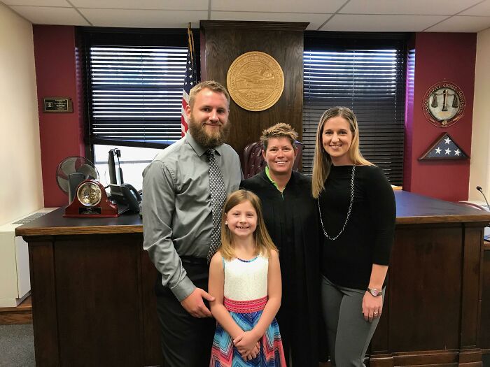 A family with a young girl and a judge celebrating their adoption story in a courtroom.