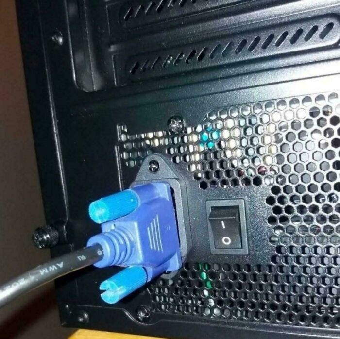 A blue VGA cable connected to a computer port with missing screws, an example of electronics fails.
