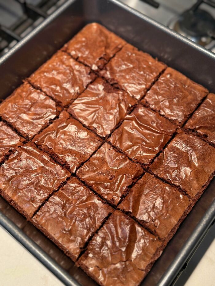 A pan of perfectly cut brownies with a shiny, crackled top, delicious treats made by talented bakers.