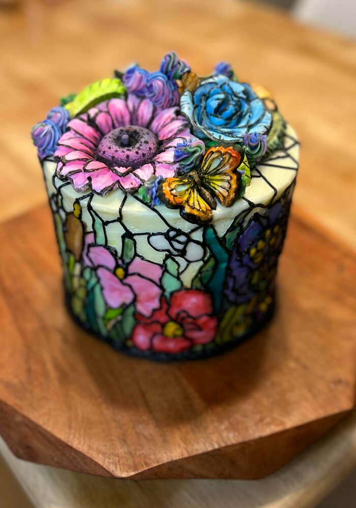 A stunning cake resembling stained glass with colorful flowers and a butterfly, an amazing treat from bakers.