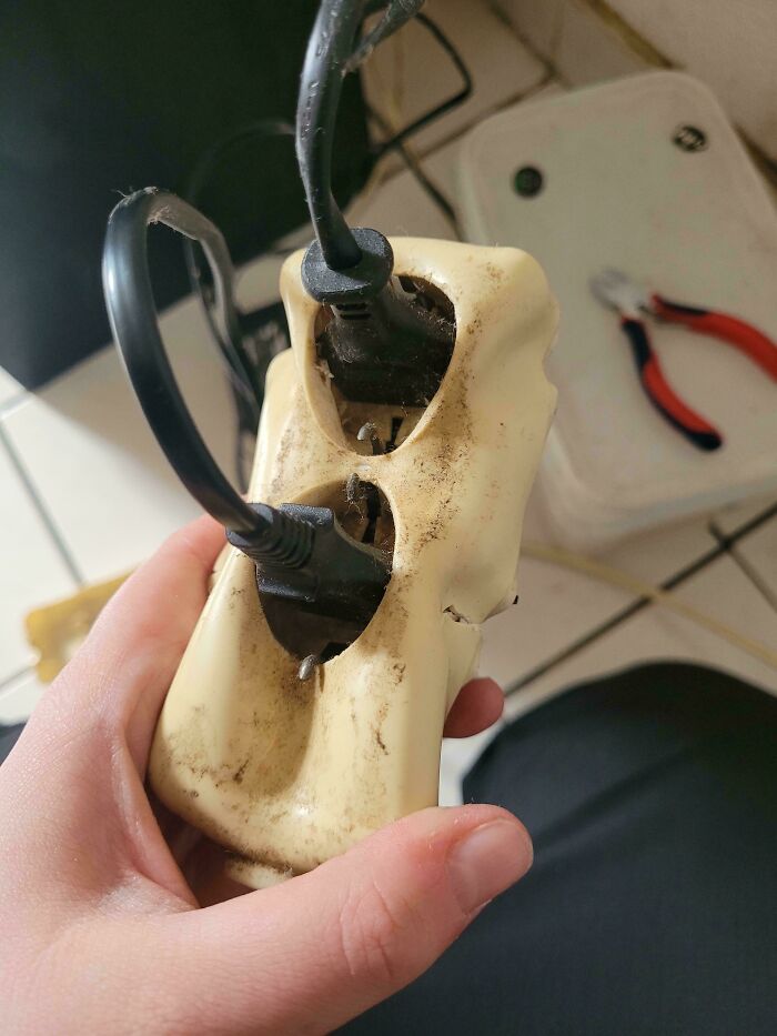 A hand holding a broken and dirty electrical outlet with wires exposed, showcasing serious electronics fails.