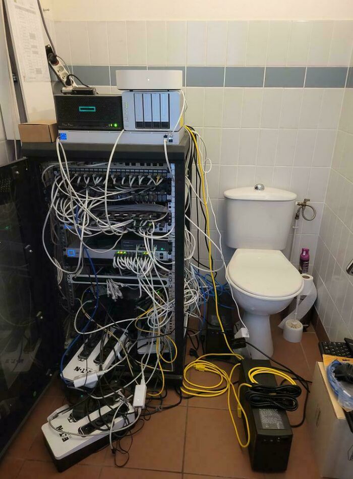 A server rack overflowing with cables next to a toilet, an alarming sight of electronics fails by IT guys.