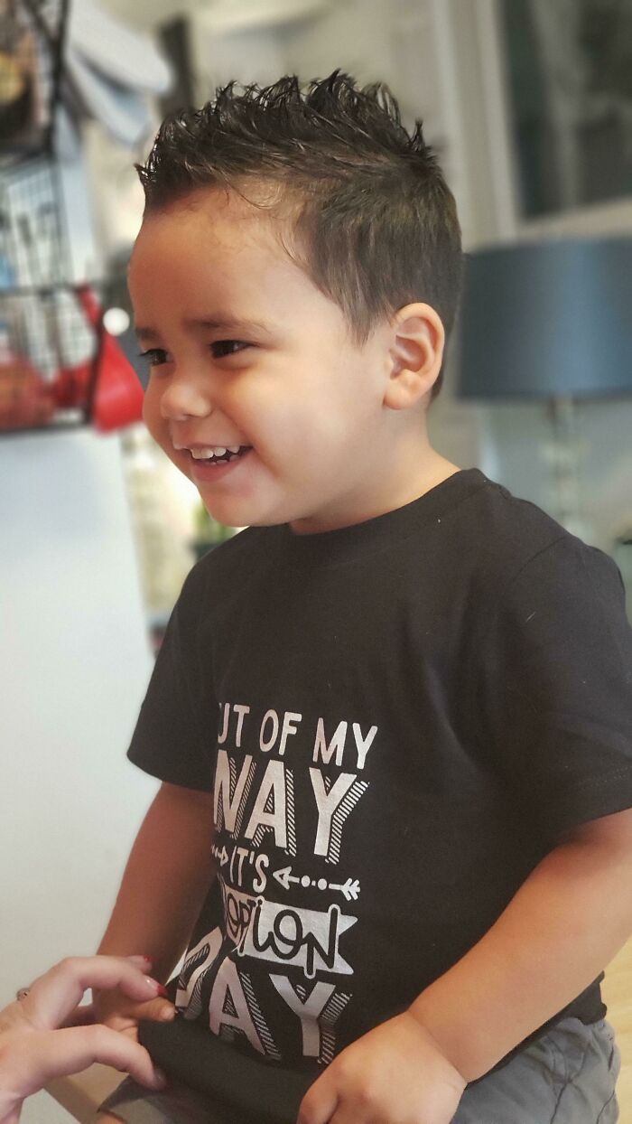 A happy young boy wearing a t-shirt that says 'It's Adoption Day,' smiling broadly, sharing adoption stories.