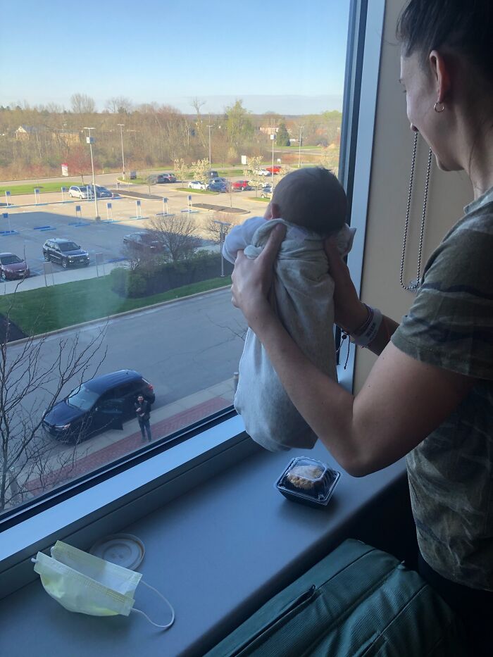 A woman holds a swaddled baby looking out a window at a parking lot, a poignant image reflecting new beginnings in an adoption story.